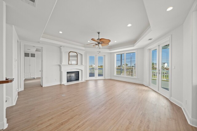 unfurnished living room with a glass covered fireplace, a tray ceiling, visible vents, and light wood-type flooring