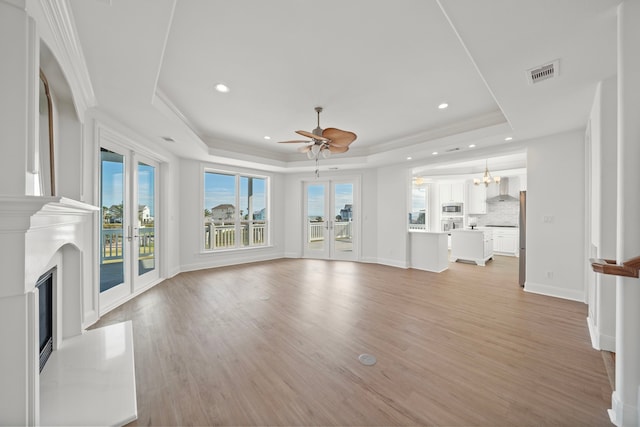 unfurnished living room with a tray ceiling, french doors, visible vents, and light wood finished floors