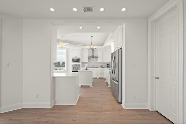 kitchen with visible vents, wall chimney range hood, appliances with stainless steel finishes, light wood-style floors, and white cabinets