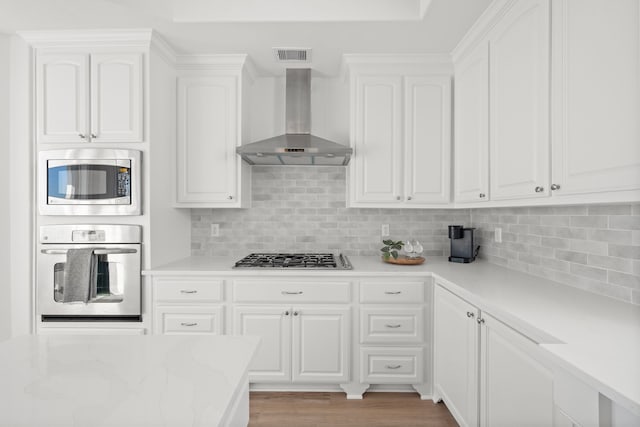 kitchen featuring visible vents, white cabinets, appliances with stainless steel finishes, and wall chimney exhaust hood