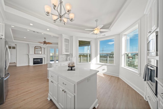 kitchen featuring white cabinetry, light wood-style floors, appliances with stainless steel finishes, a glass covered fireplace, and a raised ceiling