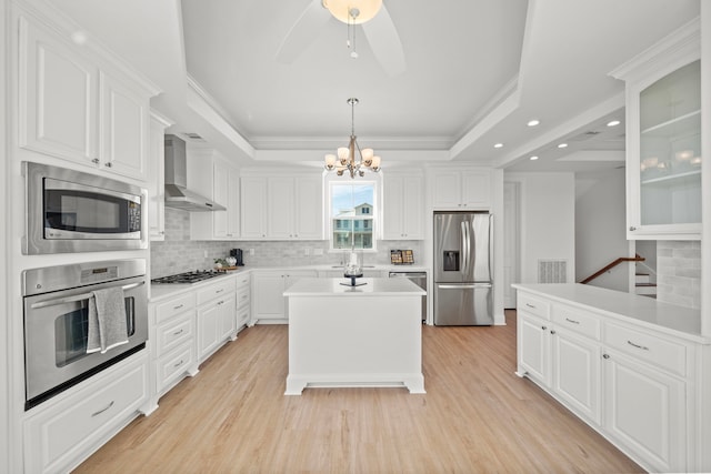 kitchen with visible vents, light wood finished floors, stainless steel appliances, a raised ceiling, and wall chimney exhaust hood