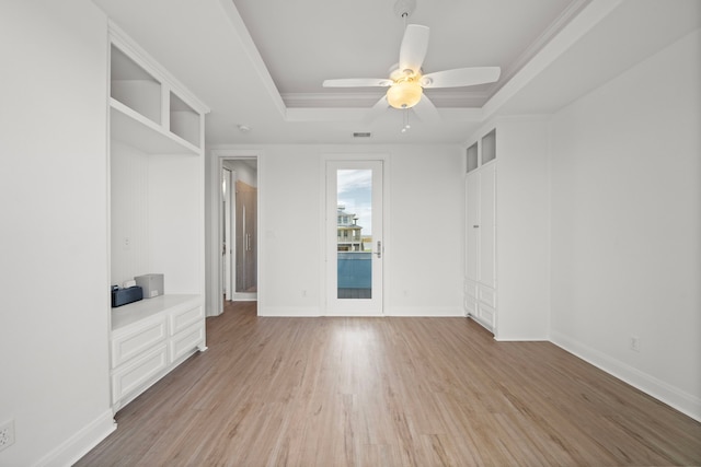 spare room with a tray ceiling, a ceiling fan, baseboards, and light wood finished floors