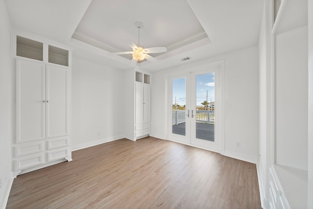 empty room featuring visible vents, a tray ceiling, french doors, light wood-style floors, and baseboards