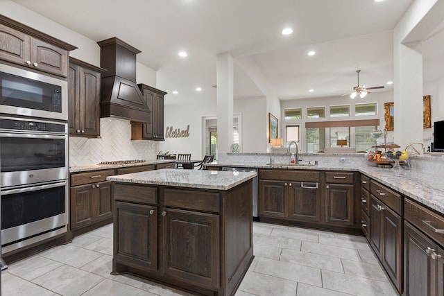 kitchen with sink, custom range hood, dark brown cabinets, kitchen peninsula, and stainless steel appliances