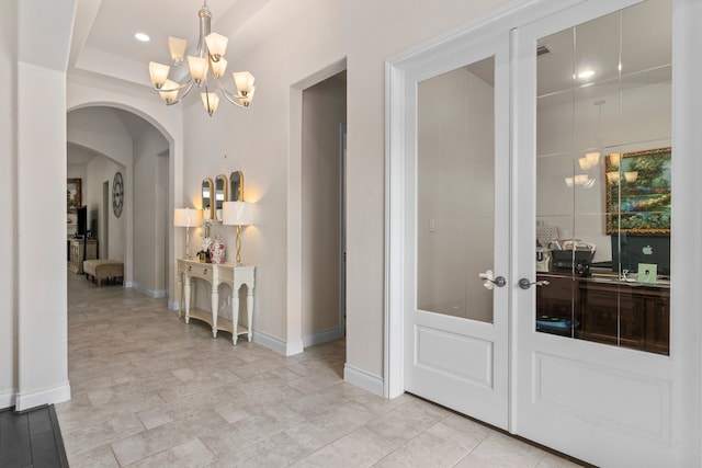 hall featuring french doors, an inviting chandelier, and a raised ceiling