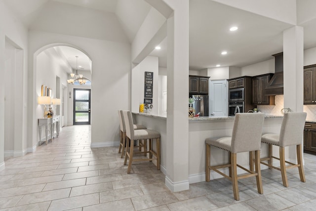 kitchen featuring appliances with stainless steel finishes, a kitchen breakfast bar, tasteful backsplash, dark brown cabinets, and an inviting chandelier