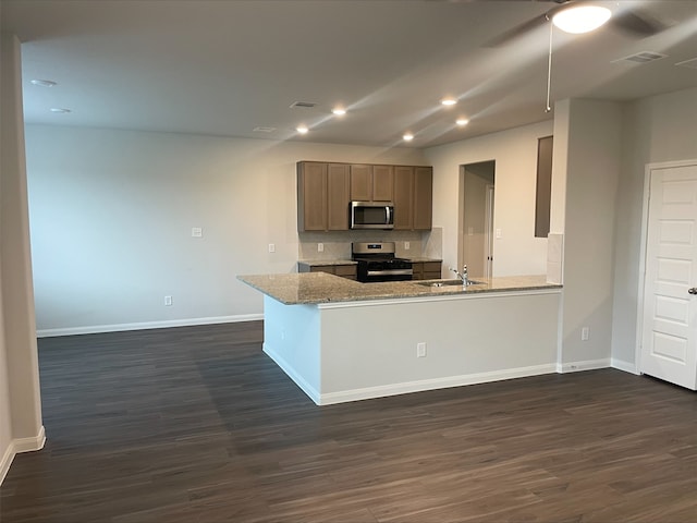 kitchen with kitchen peninsula, light stone countertops, dark hardwood / wood-style flooring, and appliances with stainless steel finishes