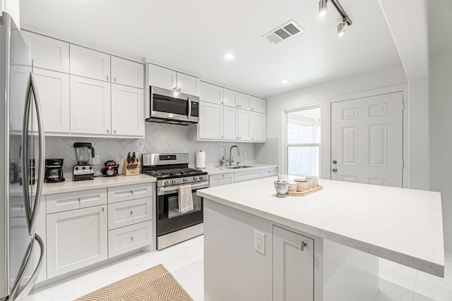 kitchen featuring decorative backsplash, appliances with stainless steel finishes, sink, a center island, and white cabinetry