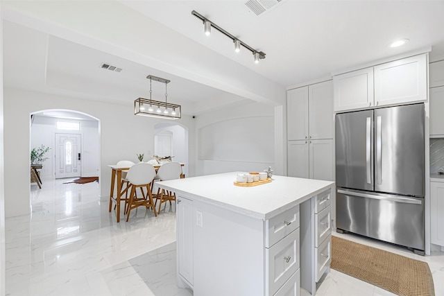 kitchen with a center island, white cabinetry, hanging light fixtures, and stainless steel refrigerator