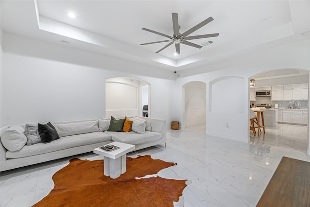 living room with a raised ceiling and ceiling fan