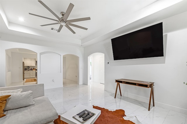 living room featuring a raised ceiling and ceiling fan