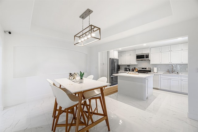 kitchen with white cabinets, appliances with stainless steel finishes, a tray ceiling, decorative light fixtures, and a kitchen island