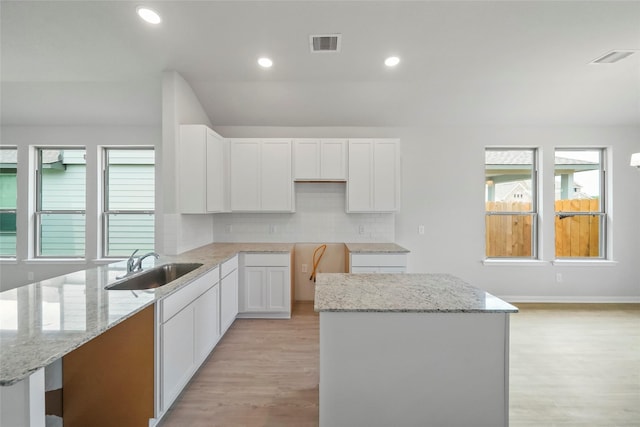 kitchen with decorative backsplash, a center island, light stone countertops, and white cabinetry