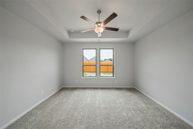 empty room featuring carpet floors, a tray ceiling, and ceiling fan