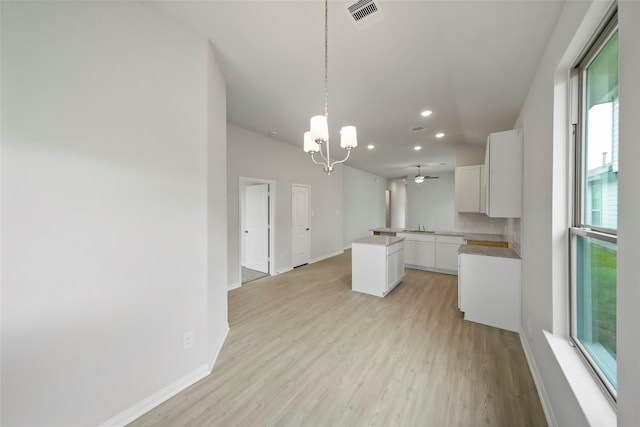 kitchen with kitchen peninsula, ceiling fan with notable chandelier, pendant lighting, white cabinets, and light hardwood / wood-style floors