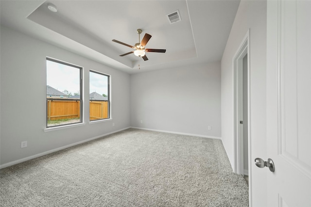 carpeted spare room with ceiling fan and a tray ceiling