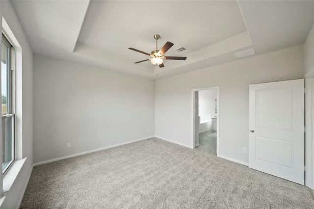 unfurnished bedroom featuring ceiling fan, a raised ceiling, carpet floors, and ensuite bathroom