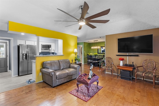 living room with ceiling fan with notable chandelier, light hardwood / wood-style floors, and a textured ceiling