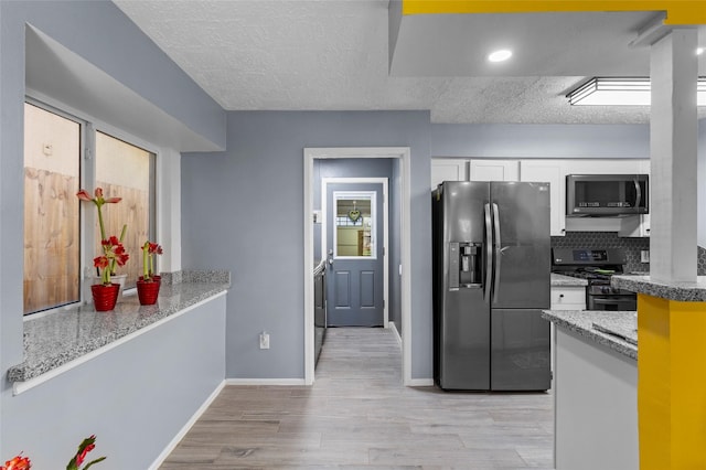 kitchen with stainless steel appliances, light stone counters, white cabinets, decorative backsplash, and light wood-type flooring