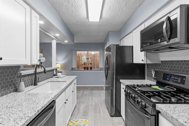 kitchen featuring sink, stainless steel appliances, light hardwood / wood-style floors, light stone countertops, and white cabinets