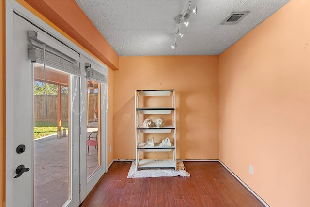 interior space with a textured ceiling, rail lighting, and hardwood / wood-style flooring