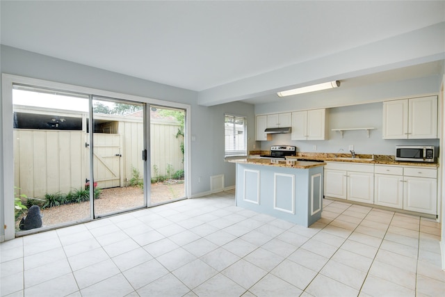 kitchen with white cabinets, a center island, light stone counters, and appliances with stainless steel finishes