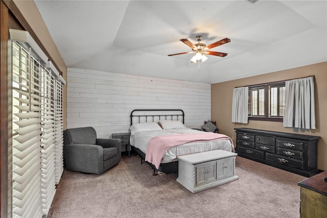 carpeted bedroom featuring ceiling fan, a tray ceiling, wooden walls, and vaulted ceiling