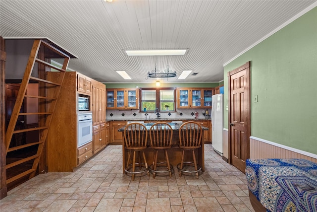 kitchen featuring a center island, white appliances, a kitchen breakfast bar, crown molding, and wooden walls