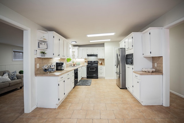 kitchen featuring black appliances, sink, decorative backsplash, light tile patterned floors, and white cabinetry