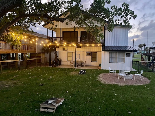 back house at dusk with a lawn, a balcony, and a patio