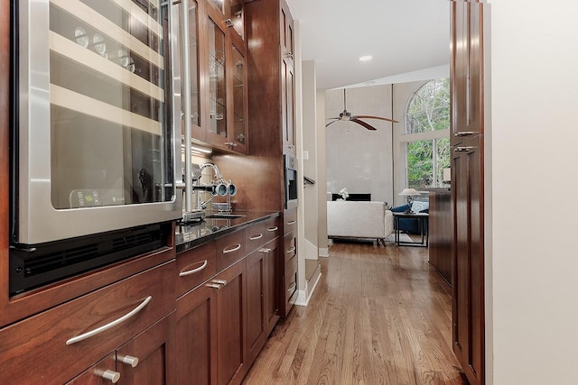 bar featuring ceiling fan, sink, dark stone countertops, light hardwood / wood-style floors, and oven