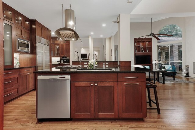 kitchen featuring island exhaust hood, a kitchen breakfast bar, light wood-type flooring, a kitchen island with sink, and built in appliances