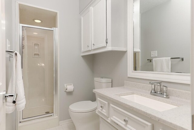 bathroom featuring tile patterned flooring, vanity, toilet, and a shower with shower door