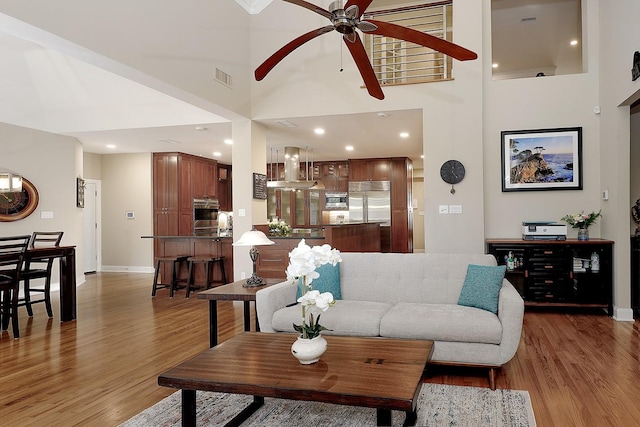 living room with hardwood / wood-style floors, a towering ceiling, and ceiling fan