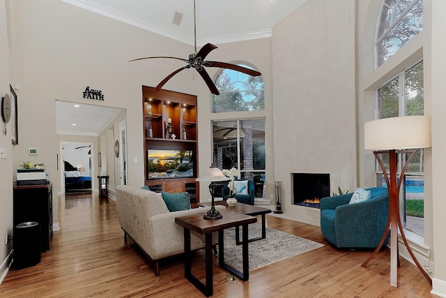 living room featuring built in shelves, a large fireplace, light hardwood / wood-style floors, and a high ceiling