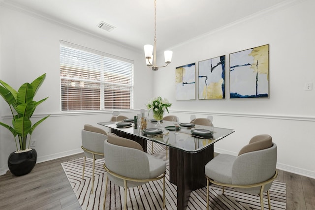 dining area with wood-type flooring, crown molding, and an inviting chandelier