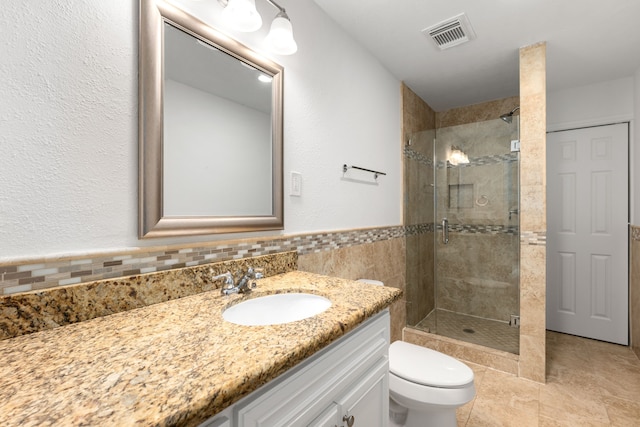 bathroom featuring a shower with door, vanity, tile walls, and toilet