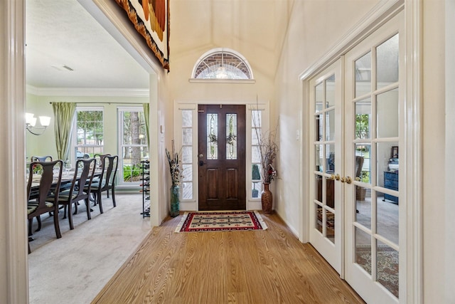 entrance foyer with french doors, ornamental molding, a notable chandelier, a towering ceiling, and hardwood / wood-style flooring