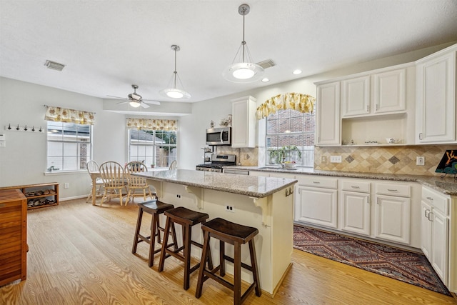 kitchen with a center island, light wood-type flooring, light stone counters, white cabinetry, and stainless steel appliances