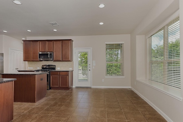 kitchen featuring decorative backsplash, appliances with stainless steel finishes, dark stone counters, dark tile patterned flooring, and a kitchen island