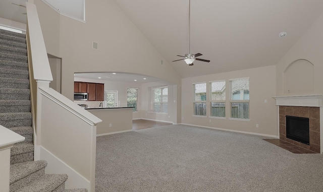 unfurnished living room with a tiled fireplace, ceiling fan, carpet floors, and high vaulted ceiling