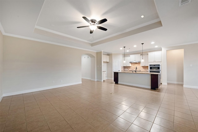 unfurnished living room with a raised ceiling and ornamental molding