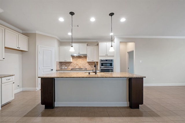 kitchen featuring pendant lighting, light stone counters, a kitchen island with sink, and sink