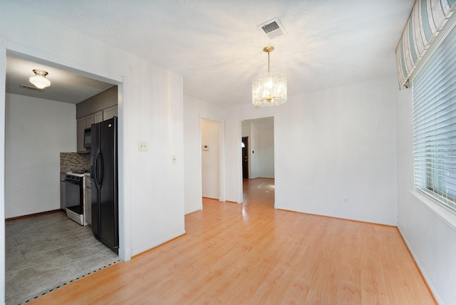 unfurnished room with a notable chandelier and light hardwood / wood-style flooring