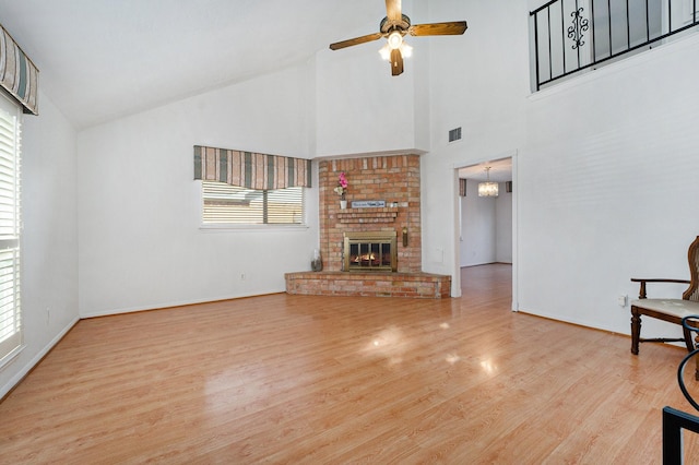 unfurnished living room featuring ceiling fan with notable chandelier, light wood-type flooring, a fireplace, and high vaulted ceiling