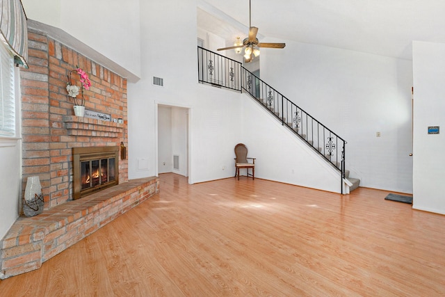 unfurnished living room with ceiling fan, wood-type flooring, a high ceiling, and a brick fireplace