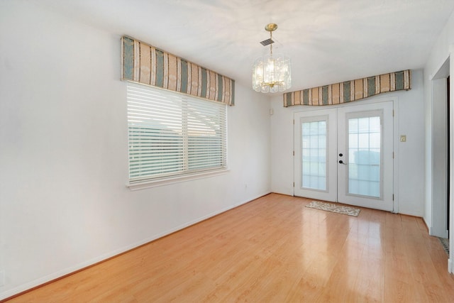 empty room with french doors, light hardwood / wood-style flooring, and an inviting chandelier