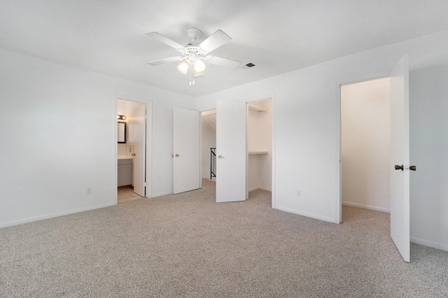 unfurnished bedroom with a walk in closet, ensuite bathroom, ceiling fan, and light colored carpet