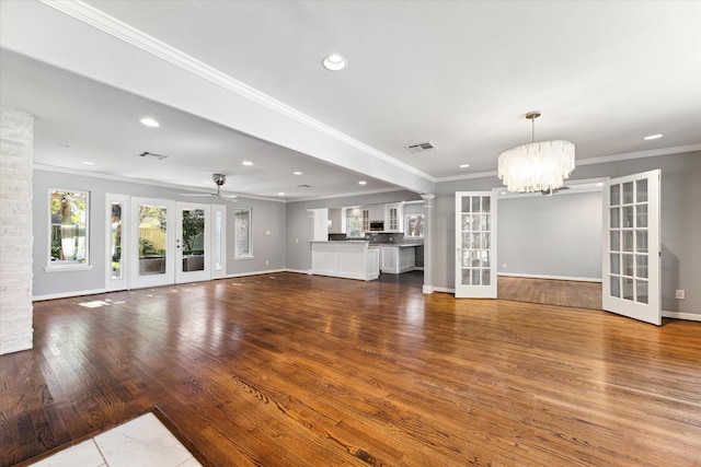 unfurnished living room with ceiling fan with notable chandelier, wood-type flooring, ornamental molding, and french doors